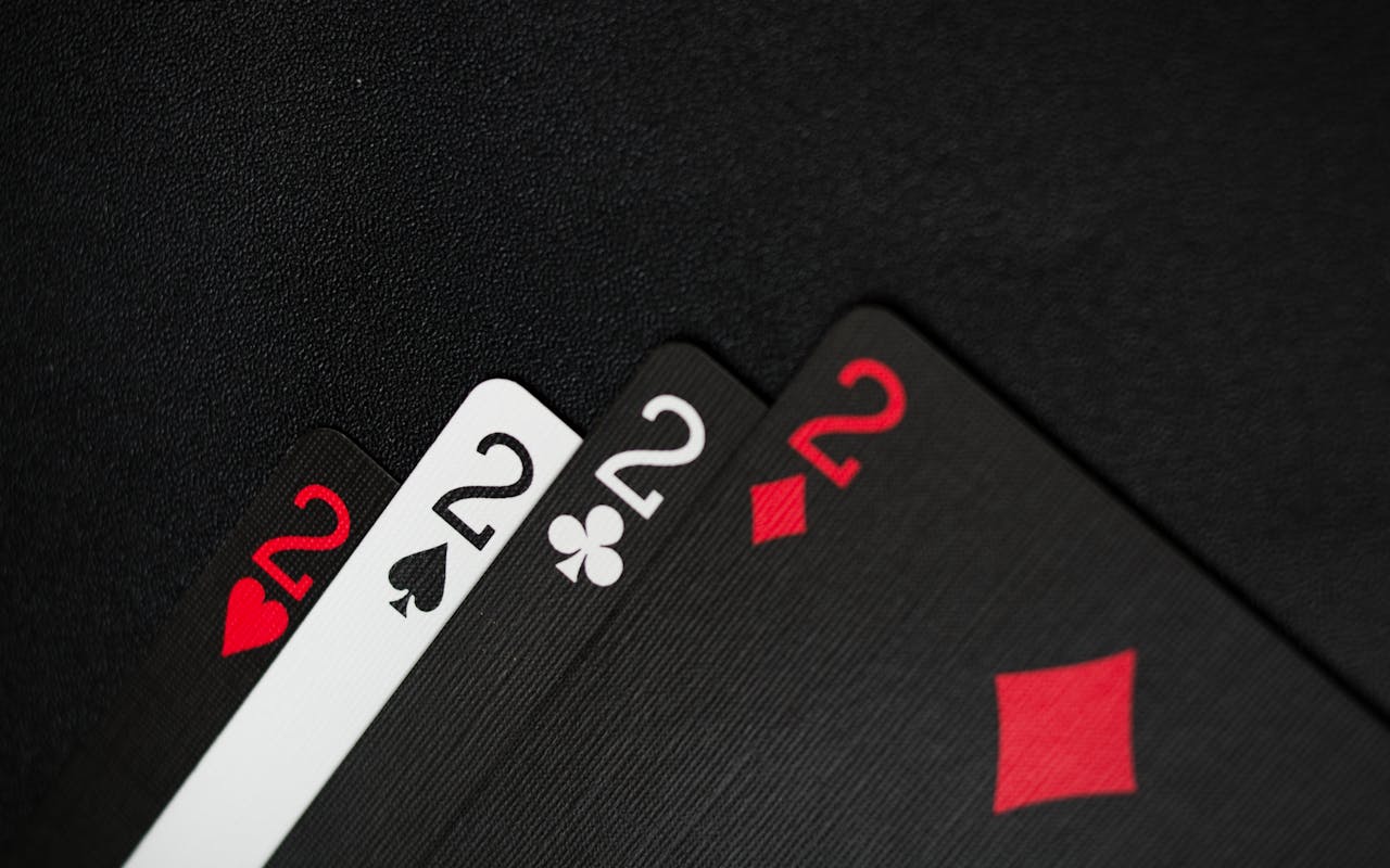 Four playing cards showing twos in various suits on a dark background.